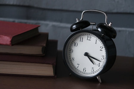 Black retro alarm clock and books on the table in the room. Loft style.