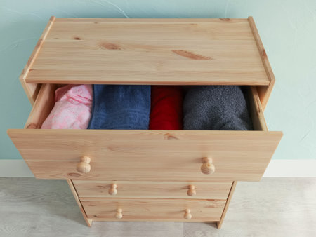 Folded towels in an open drawer of a wooden chest of drawers. Top view.