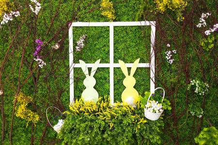 Two white Easter bunnies in a window frame with baskets against a background of green foliage. Artificial decoration.の写真素材