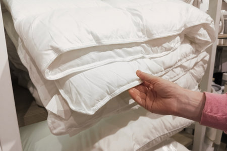 A customer's hand touches a white bed blanket in a store.の写真素材