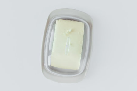 A piece of butter in a plastic butter dish with a transparent lid. White background.の写真素材