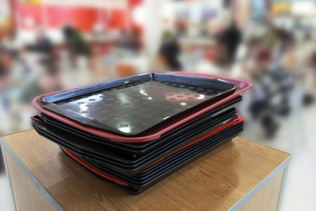 Black plastic trays stacked on table in self-service restaurant. Focus on foreground.