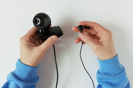 Webcam and wired microphone in hands of Caucasian woman. White background.