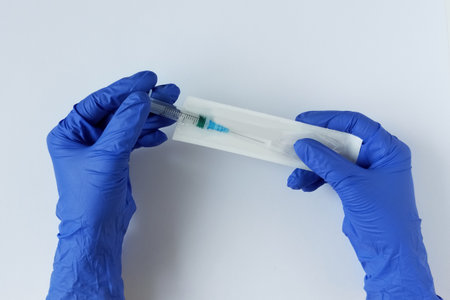 Hands with blue medical gloves. Takes out a syringe from a vacuum package. White background