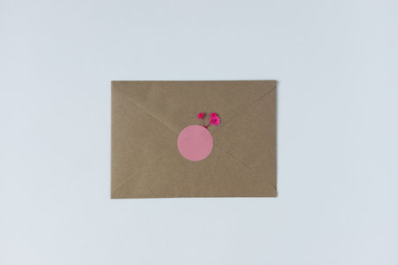Sealed kraft envelope decorated with pink round sticker and small flowers. White background.の写真素材
