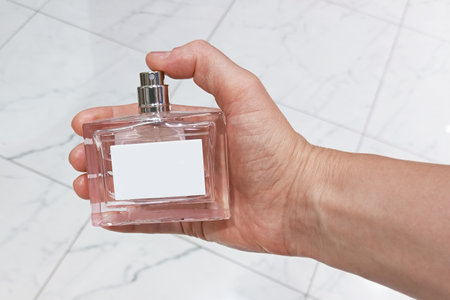 Glass bottle of perfume in hand of Caucasian woman against tiled floor background.