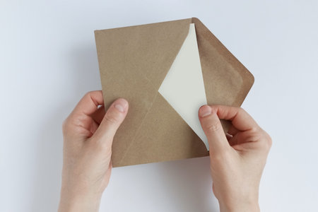 Takes out a white blank postcard from a kraft envelope. Postal envelope in hands. White background.
