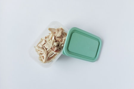 Pieces of chicken fillet in a plastic container with an open lid. White background.