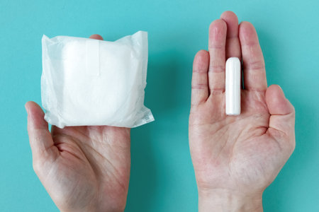 Feminine sanitary pad and tampon for intimate hygiene in packaging on the palms of a Caucasian woman. Turquoise background.の写真素材