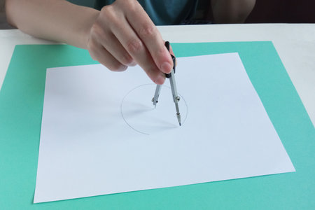 Drawing a circle with a compass on a white sheet of paper. Caucasian woman at the table close-up.の写真素材