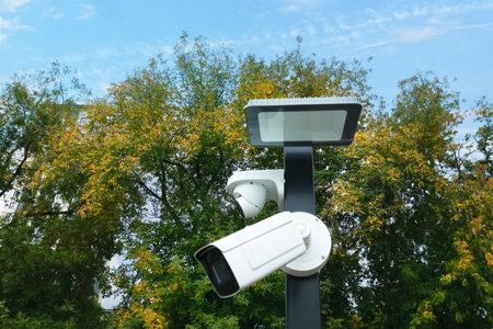 Two white surveillance cameras on a pole against a background of trees.