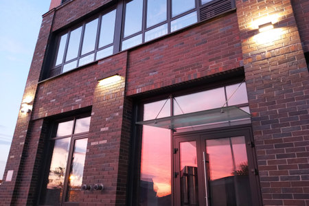 A burgundy brick wall of a residential building with windows and streetlights. The red sunset is reflected in the glass windows.の写真素材