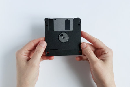 A Caucasian woman holds a computer floppy disk. White background. Top view.