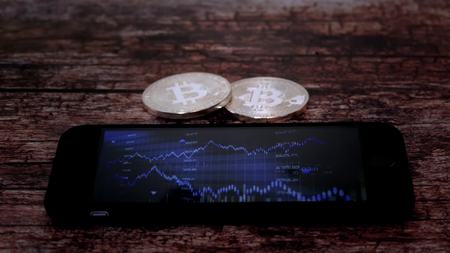 Two coins bitkoyn, lying next to the smartphone, on the screen which displays a chart of quotations, crypto currency.の写真素材