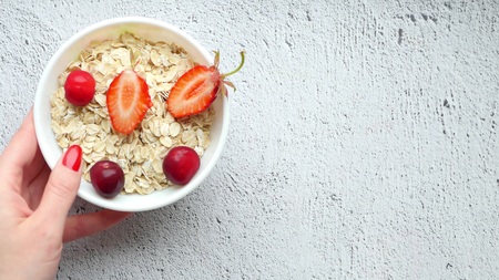 Beautiful female hands lay out on the table a composition of bright berries - 2. Juicy red cherries on a white background. Bowl of oatmeal. Healthy breakfast. Proper nutrition. Fault on the table.の写真素材