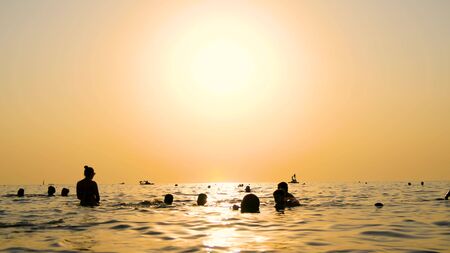 A group of people swimming in the sea on the beach at sunset.の写真素材