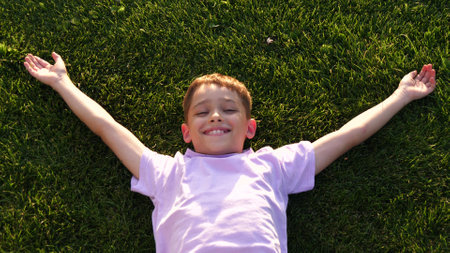 Wonder and Joy. happy smile child lay in grass. child open arms lay green grass park. aerial view....