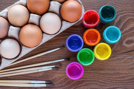 Easter eggs in an egg box on a wooden background, paint for drawing, brushes. Preparation for the celebration of Easter. Art work, handwork, creativity for Easter decoration.の写真素材