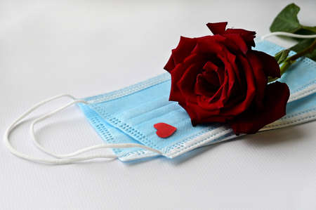 Disposable medical face mask with red heart and red rose on white background. Safe Valentine's Day...