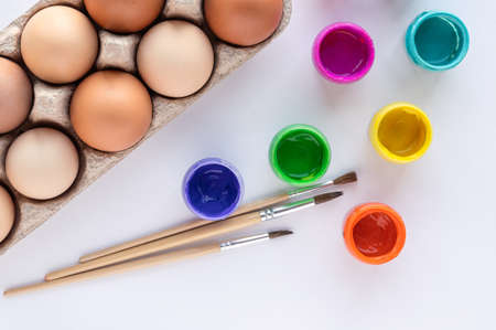 Easter eggs in an egg box on a white background, paint for drawing, brushes. Preparation for the celebration of Easter. Art work, handwork, creativity for Easter decoration.の写真素材