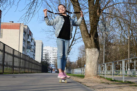 cute girl in jeans and pink sneakers rides a penny skate longboard around the city. International...