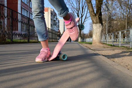Close-up legs of girl skateboarder in blue jeans and pink sneakers, riding pink penny skate...