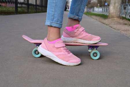 Close-up legs of girl skateboarder in blue jeans and pink sneakers, riding pink penny skate longboard. International Skateboarding Day. Selective focusの写真素材