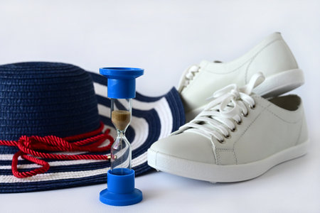 beautiful women's hat with a large brim, white summer shoes, sneakers and an hourglass on a white background. The concept of summer holidays. Travel time.の写真素材