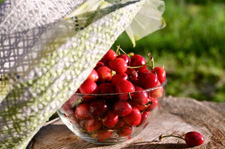 in summer garden glass vase with ripe, juicy cherry is covered with hat on stump. Delicious and healthy food. Close-upの写真素材