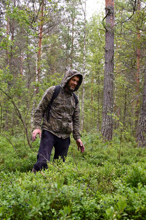 man in camouflage clothing with a backpack in the woods. A forester walks along a path through a dense forestの写真素材