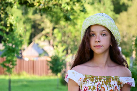 Portrait of a pretty girl with long wavy hair in a hat on the background of a rural landscape....