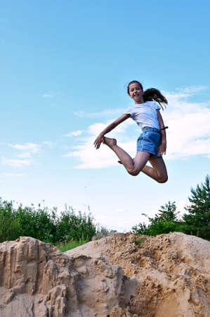 cute cheerful girl makes a jump in air against background of blue sky. Female athlete in white...