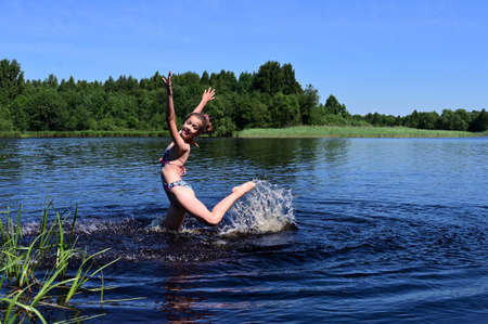 pretty cheerful girl in swimsuit is having fun in river and creates splashes on water. Summer outdoor recreation, a healthy lifestyle. Copy spaceの写真素材