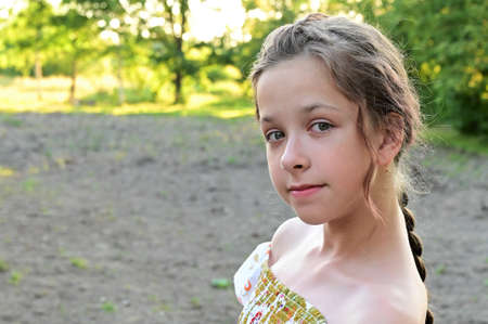 Portrait of beautiful young girl with long hair braided in braid, dressed in summer dress against background of green foliage. Summer outdoor recreation. Copy spaceの写真素材