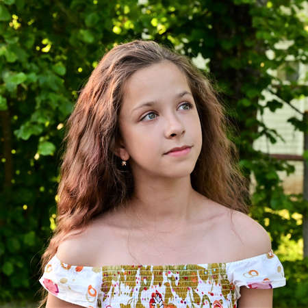 Portrait of beautiful young girl with long wavy hair in summer dress on background of green foliage. Summer outdoor recreationの写真素材