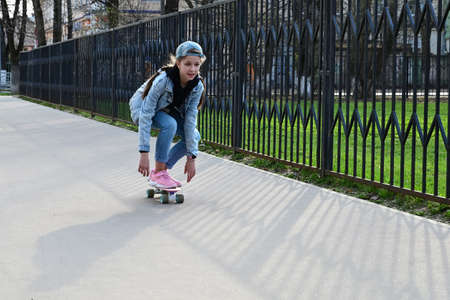 cute girl in jeans and pink sneakers rides a penny skate longboard around the city. International Skateboarding Day. Sports and Development Conceptの写真素材