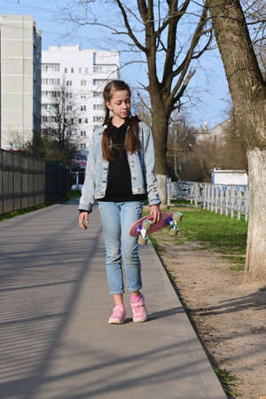 beautiful girl in denim clothes and pink sneakers. In the hand of a penny board, a longboard. International Skateboarding Day. Sports and development concept, lifestyleの写真素材