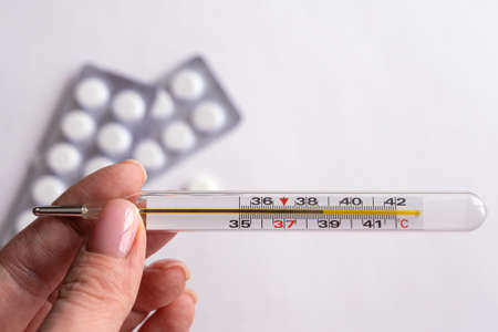 thermometer in a woman's hands. The pills are on the table. Close-up on a white backgroundの写真素材