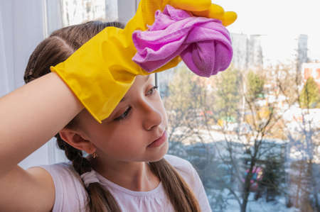 girl in yellow household gloves cleans the window with a pink napkin. Cleaning concept. Fatigueの写真素材