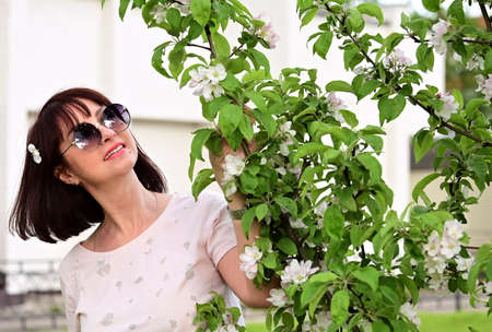 beautiful woman in sunglasses with dark hair among the white flowers of a blooming apple tree