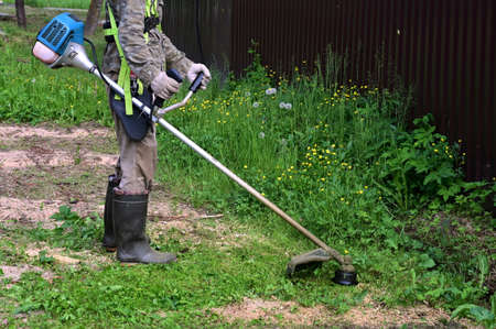 man in special protective clothing with lawn mower in his hands mows grass. Gardener cuts grass with trimmer, brushcutter mower or power tool for mowing lawnの写真素材