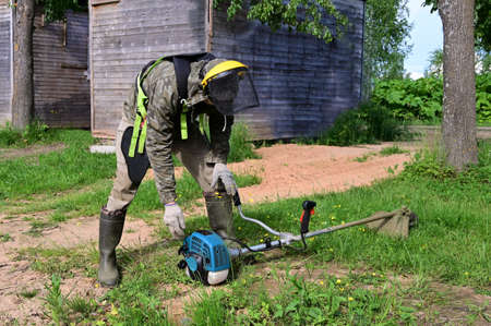 worker in special protective clothing with lawn mower in his hands mows grass. Trimer mows lawn....