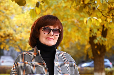 beautiful mature elegant woman in stylish jacket in autumn park on background of yellow leaves. Close-up. Hello, autumn! Outdoor recreationの写真素材