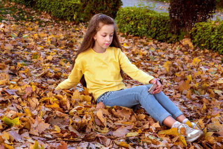beautiful girl in a yellow jumper and jeans is sitting among autumn leaves and enjoying nature. Outdoor recreationの写真素材