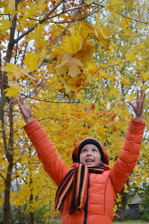 pretty girl in an orange jacket, beret and scarf walks in beautiful autumn park and throws up yellow...
