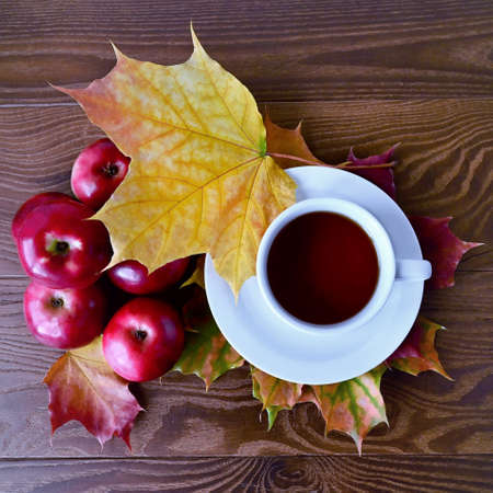 Autumn composition of red apples and yellow maple leaves lying on wooden table and white cup of tea. Flat lay with top viewの写真素材