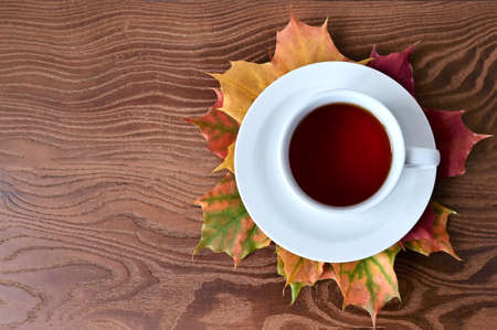 Autumn composition of white cup of tea and colorful maple leaves on wooden table. Concept of autumn, home comfort and warmth. Flat lay with top viewの写真素材