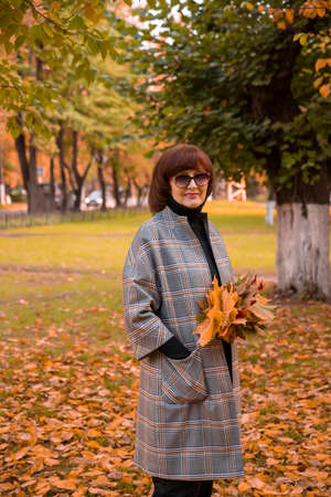 beautiful mature elegant woman walks in an autumn park with yellow maple leaves in her hands. Hello autumn!の写真素材