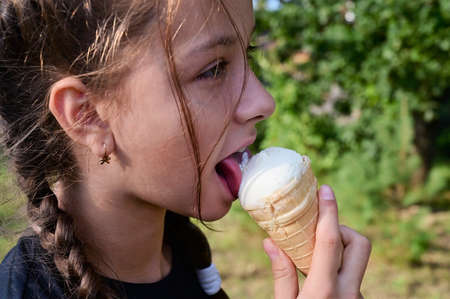 cute girl eats ice cream in waffle cone on background of green forest. Problem of hot climate and global warming. Close-upの写真素材