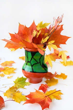 A beautiful bouquet of yellow and orange maple leaves in ceramic vase on white background. Bright colors of autumnの写真素材